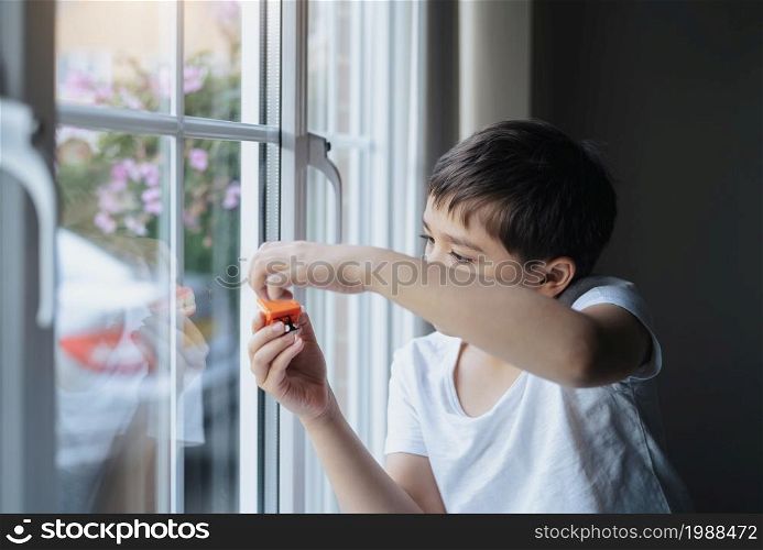 Kid playing with toy and looking at the midge climbing up outside of double glazed window. Boy sitting next to window looking out at insect with thinking face,Children learning about animals life in nature