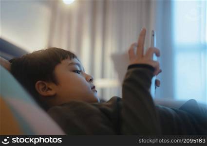 Kid reading bed time stories on tablet before sleep, Happy boy lying in bed playing games on digital pad, Portrait Child relaxing at home in his bed room on weekend.