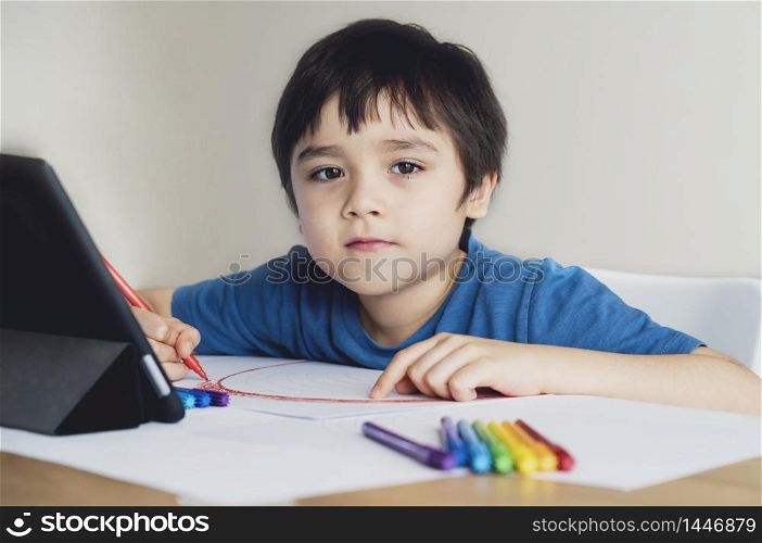 Kid red pen colouring rainbow on paper,Child using digital tablet for homework online lesson,Boy enjoy art activity at home, self-isolation, online education, home schooling, distance learning concept