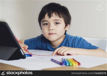 Kid red pen colouring rainbow on paper,Child using digital tablet for homework online lesson,Boy enjoy art activity at home, self-isolation, online education, home schooling, distance learning concept