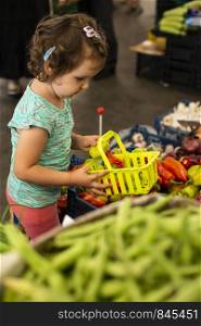 Kid shopping in vegetable market. Child collect peppers in basket.