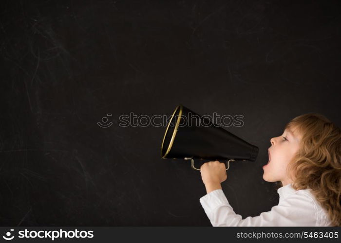 Kid shouting through vintage megaphone against blackboard