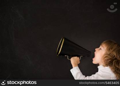 Kid shouting through vintage megaphone against blackboard