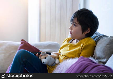 Kid sitting on sofa holding remote control, Candid short child boy relaxing at home watching TV ,Active children while school break in the summer.social Distance, E-learning online education