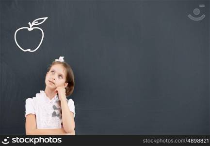 Kid student girl against school blackboard having good idea. Thoughtful girl standing at blackboard