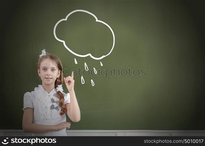 Kid student girl against school blackboard pointing with finger up. School girl at table