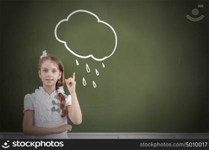 Kid student girl against school blackboard pointing with finger up. School girl at table