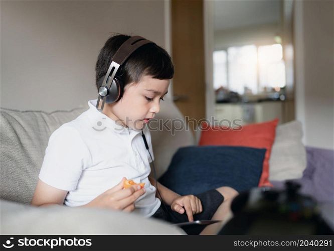Kid wearing headphone listening to music,Child boy doing homework by using digital tablet searching information on internet,E-learning, New normal life,Children with social network concept