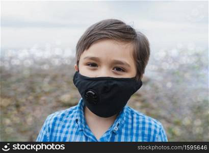 Kid wearing protective face mask for pollution or virus, Mixed race asian - caucasian 6 year old, Child wearing protection mask while playing outside, Concept for Covid 19 or Coronava virus outbreak