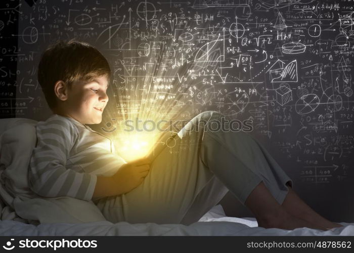 Kid with tablet pc. Little cute boy sitting in bed and using tablet