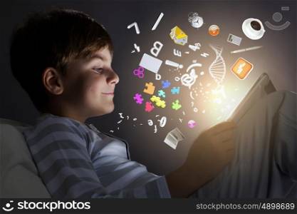Kid with tablet pc. Little cute boy sitting in bed and using tablet