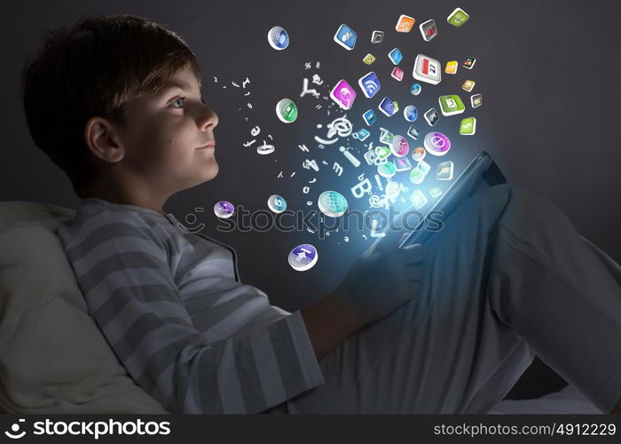 Kid with tablet pc. Little cute boy sitting in bed and using tablet