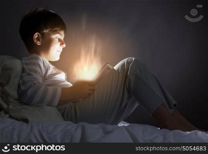 Kid with tablet pc. Little cute boy sitting in bed and using tablet