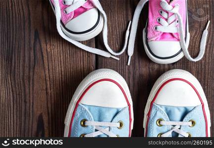 kids and adults textile sneakers on a brown wooden background, top view