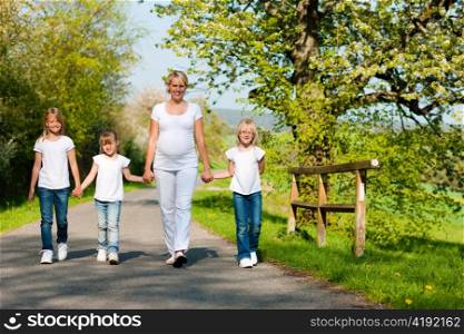 Kids and her mother walking down a path in spring, the mother is pregnant