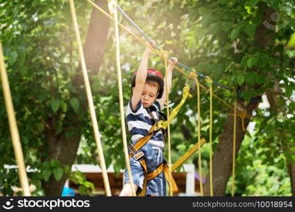 Kids climbing in adventure park. Boy enjoys climbing in the ropes course adventure. Child climbing high wire park. Happy boys playing at adventure park, holding ropes and climbing wooden stairs.