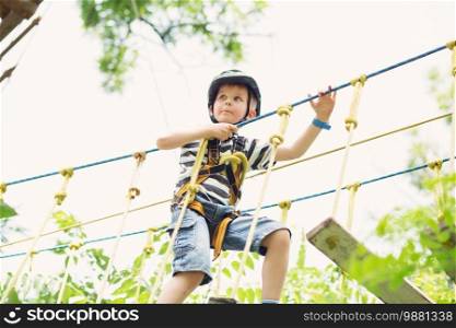 Kids climbing in adventure park. Boy enjoys climbing in the ropes course adventure. Child climbing high wire park. Happy boys playing at adventure park, holding ropes and climbing wooden stairs.