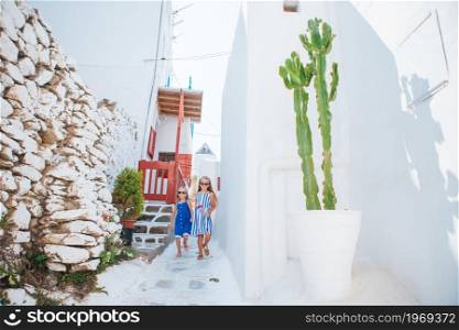 Kids having fun outdoors at street of typical greek traditional village on Mykonos streets. Family vacation in Europe. Father and kids at street of typical greek traditional village on Mykonos Island, in Greece