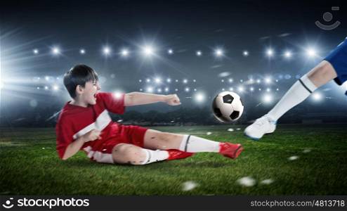 Kids play soccer on stadium . Kid boy in red uniform on soccer stadium kicking ball
