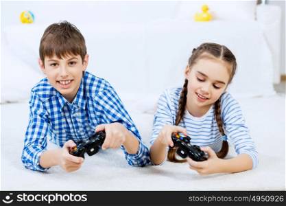 Kids playing game console. Cute kids lying on floor playing games on joystick