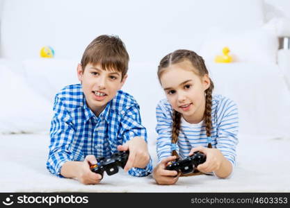 Kids playing game console. Emotional kids lying on floor playing games on joystick