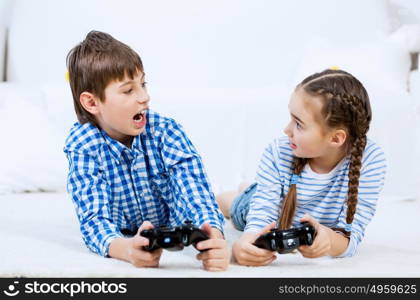 Kids playing game console. Emotional kids lying on floor playing games on joystick