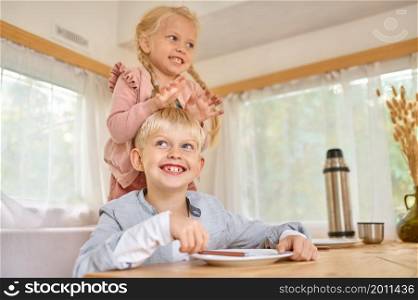 Kids poses on the kitchen in motorhome, summer camping. Family with children travel in camp car, trailer interior on background. Campsite adventure, travelling lifestyle, boy and girl in rv car. Kids poses on kitchen in motorhome, summer camping