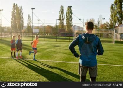 Kids practicing soccer on grass field under football coach control. Group of young boys exercising on stadium at summer day. Kids practicing soccer on grass field under football coach control