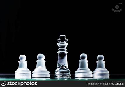 King and several pawns on chessboard in dark background. Hierarchy concept.
