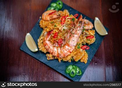 King prawn Paella Spanish seafood Paella rice with red and green pepper chili on black stone plate on wood table