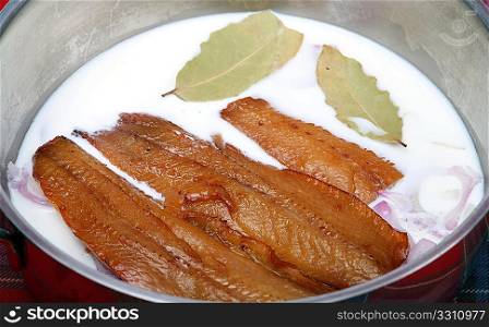 Kippers in a saucepan with milk, bay leaves, and onion, ready for braising.