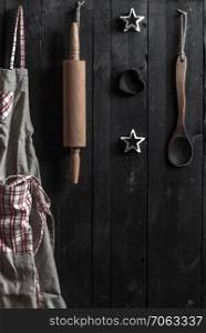 Kitchen apron, rolling pin and other kitchen tools hanged from nails on a wooden wall