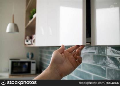Kitchen interior with modern furniture. The man opens a modern hanging cabinet for a kitchen without door handles, with a margin of 2 cm at the bottom for hands. Kitchen interior with modern furniture. The man opens a modern hanging cabinet for a kitchen without door handles