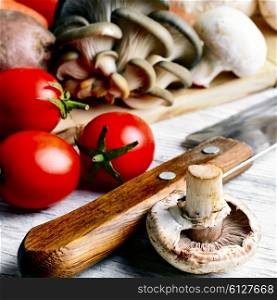 Kitchen knife,mushrooms of two varieties,the tomatoes on light wooden background