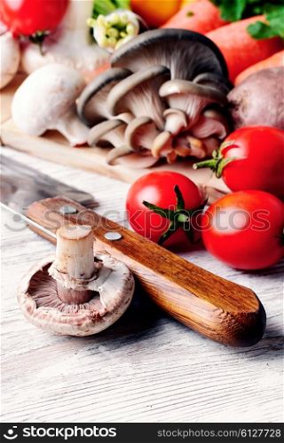 Kitchen knife,mushrooms of two varieties,the tomatoes on light wooden background