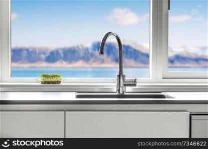 Kitchen sink by a window with a view over the sea and mountains with green cress growing