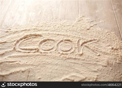 Kitchen table filled with flour and written word cook on it