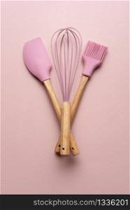 Kitchen tools as brush, whisk and spoon on pink table. Flat lay with clean kitchen utensils.