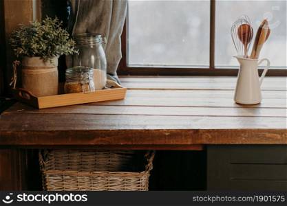 Kitchen utensils in white container on wooden table near window. Home kitchen decor. Kitchenware. Time to cook. Cutlery in room.