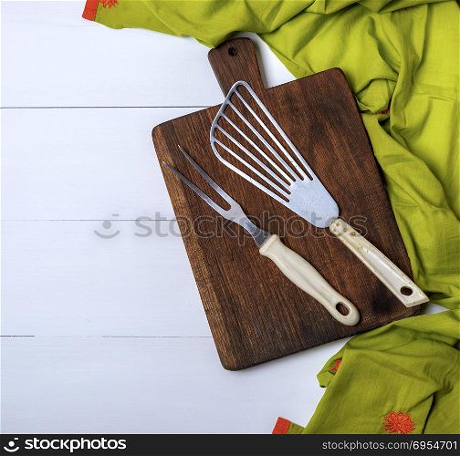 kitchen vintage fork and scapula on a brown wooden board and green towel on a white table, empty space on the left