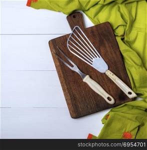 kitchen vintage fork and scapula on a brown wooden board and green towel on a white table, empty space on the left