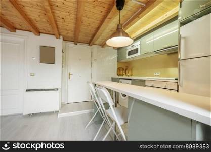 Kitchen with shiny pale green wooden furniture combined with white wooden countertop, ceramic hob and stainless steel extractor hood and coffered pine wood ceiling