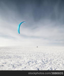 Kite surfer being pulled by his kite across the snow. Kiteboarder with blue kite on the snow