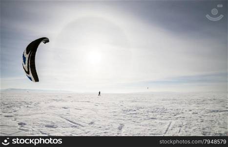Kite surfer being pulled by his kite across the snow. Kiteboarder with blue kite on the snow