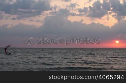 Kite surfer sailing on the sea at sunset