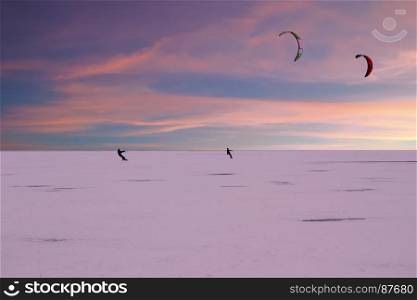 Kite surfers on frozen lake in the countryside from the Netherlands in winter at twilight