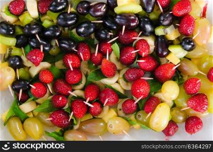 kiwi, banana, strawberries, grapes, cheese impaled on skewers on a plate