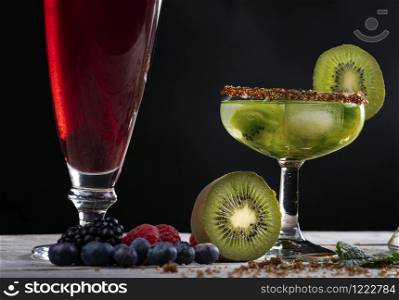 Kiwi cocktail decorated with slices and fruits of the forest on a wooden base.