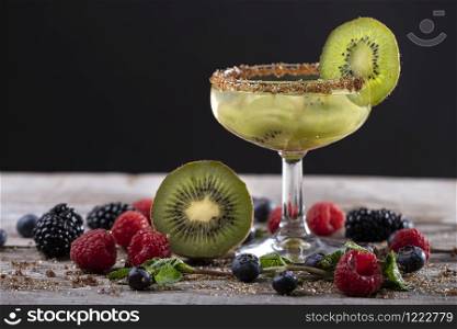 kiwi cocktail on a wooden base decorated with fruits of the forest