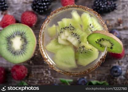 kiwi cocktail seen from above decorated with fruits of the forest on a wooden background